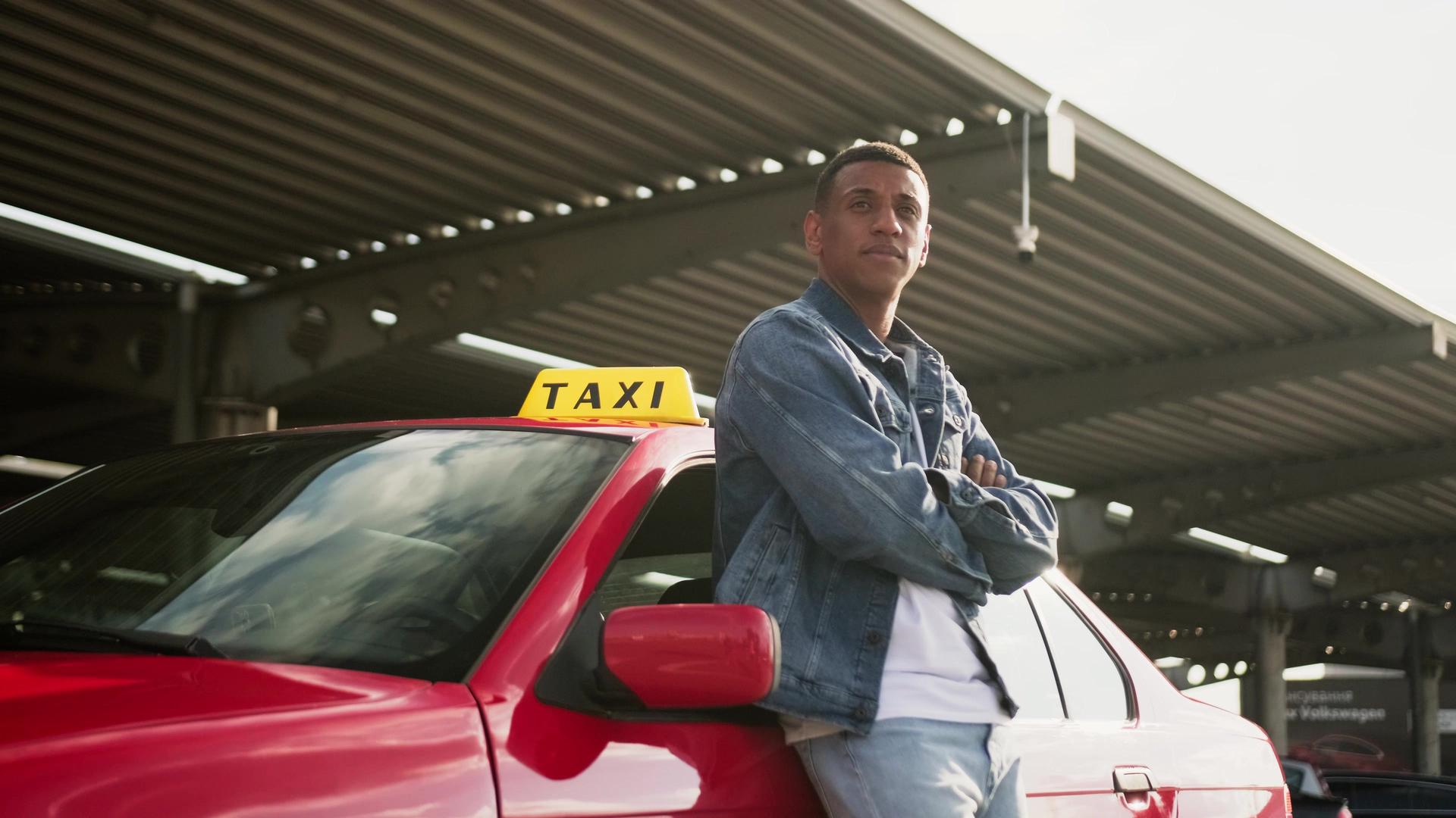 Male taxi driver standing near car with arms crossed on the parking.
