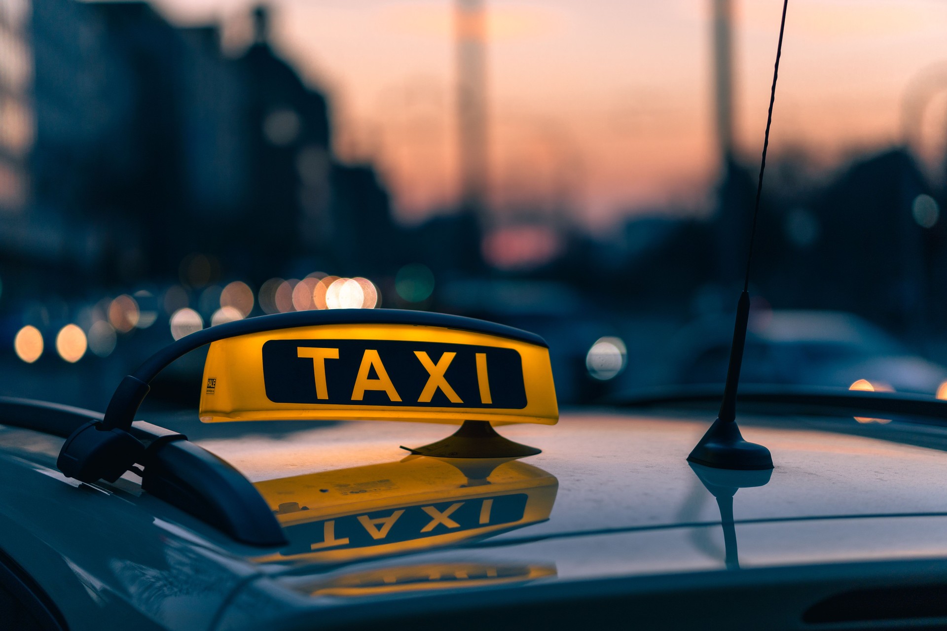 A close-up shot of a taxi sign in the warm colours of sunset with bokeh lights in the background.